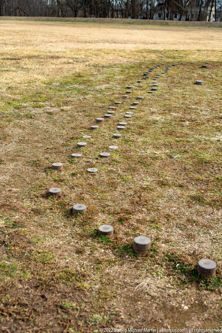 A diagonal line of small circular markers crosses a broad grassy lawn.
