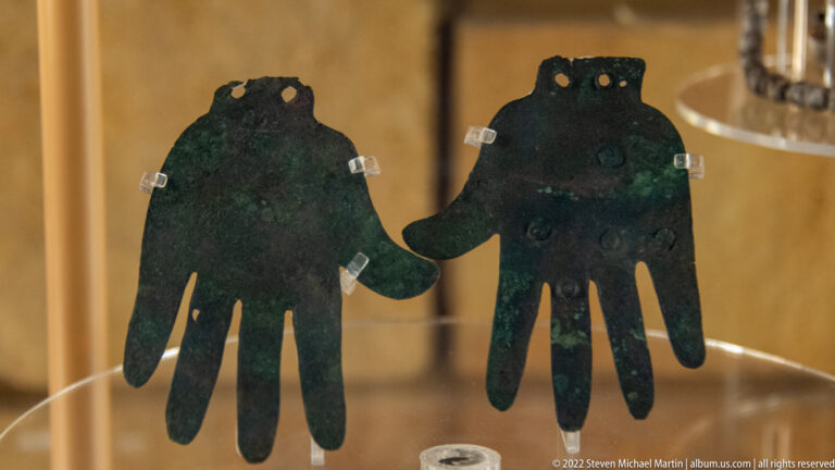 Two hand-shaped green copper cutouts stand side by side on clear supports inside a case.