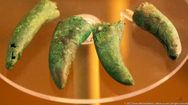 Four curved green copper pieces are arranged in a row against an orange museum display background.