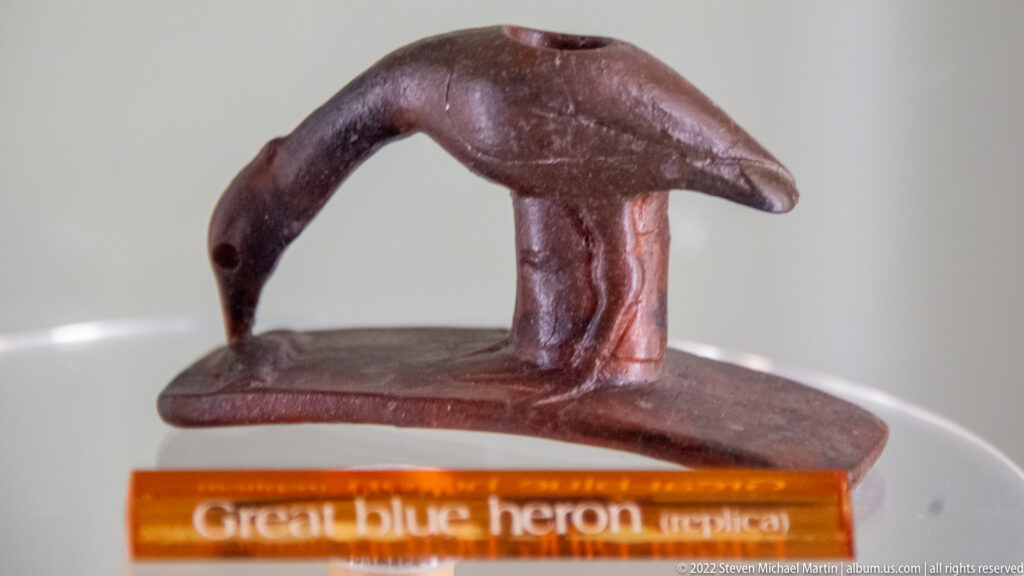 Dark brown heron-shaped pipe replica with a curved neck and raised bowl opening.
