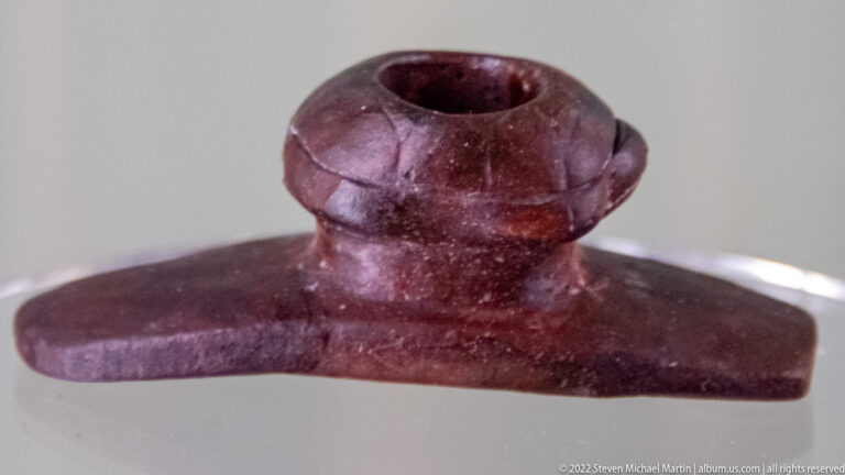 Dark purple-brown stone pipe with a round opening above a broad horizontal base.