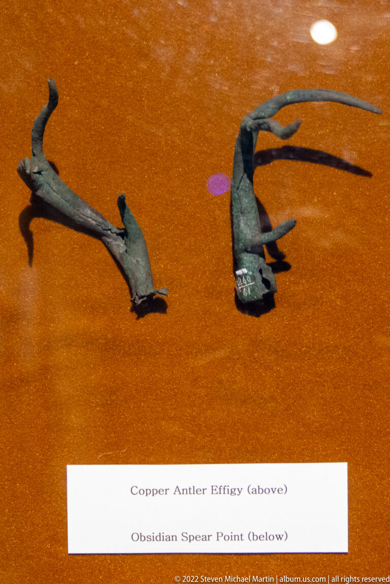 Two dark artifacts on orange backing, labeled as a copper antler effigy and an obsidian spear point.