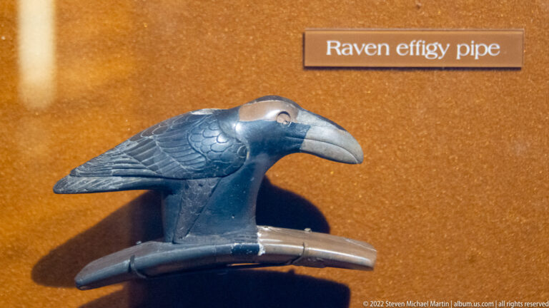 Close view of a dark raven effigy pipe with incised feathers, a bright eye and hooked beak.