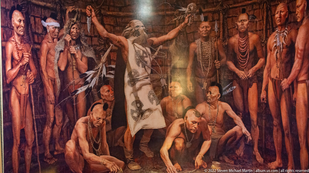 Mural of a central standing figure surrounded by people, with several kneeling in the foreground.