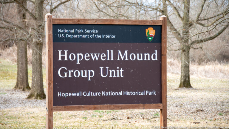 Brown park sign naming the Hopewell Mound Group Unit stands among leafless trees.