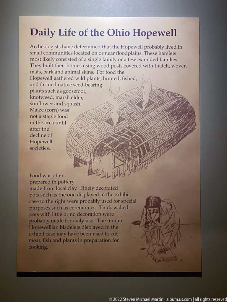 A panel about Ohio Hopewell life includes a drawing of a large timber dwelling and a person preparing food.