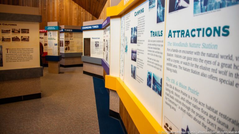 A gallery corridor lined with panels about trails, camping, and local attractions recedes into the distance.