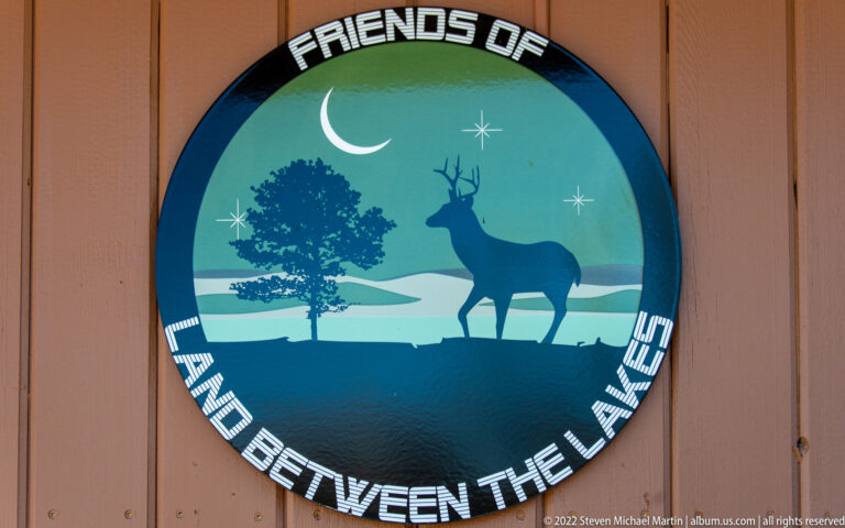 A circular emblem shows a deer and tree beside a crescent moon above blue water.