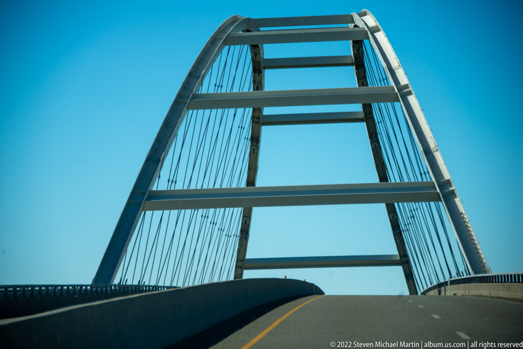 Steel bridge beams rise overhead above a roadway with a yellow centerline.