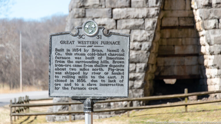 A Great Western Furnace marker stands before the dark opening of a stone furnace.