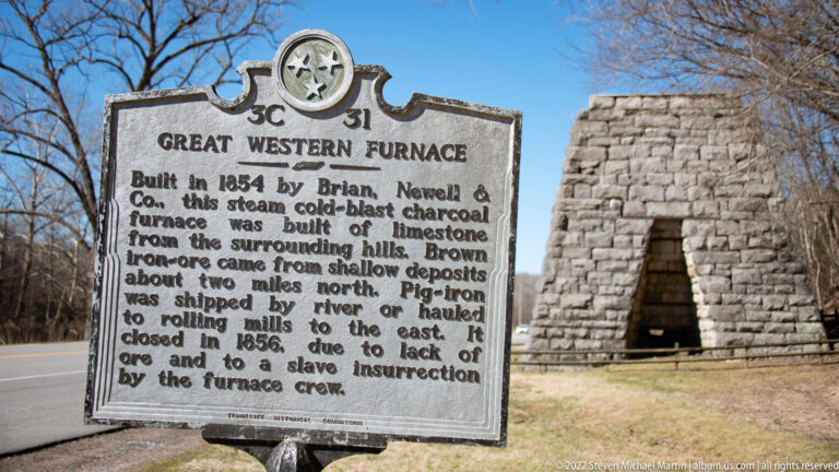 A historical marker stands in front of the rough stone furnace and its tall opening.