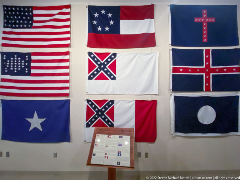 Rows of Civil War-era flags hang above an interpretive stand in a museum gallery.