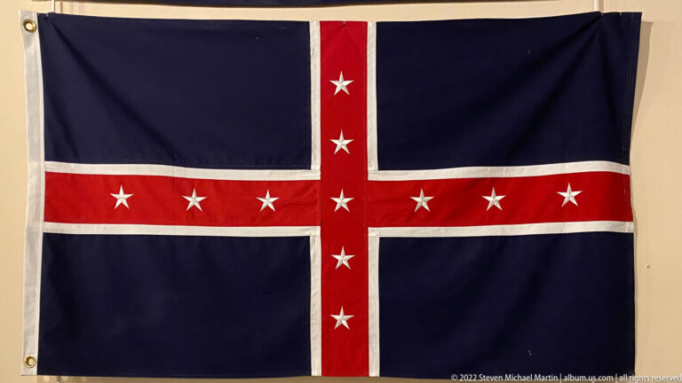 A dark blue flag has a white-edged red cross and rows of white stars.