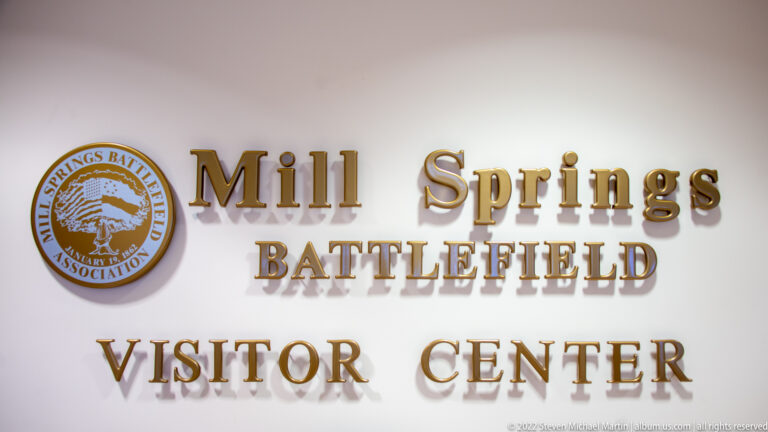 Raised gold visitor center lettering and a circular battlefield association emblem on a pale wall.