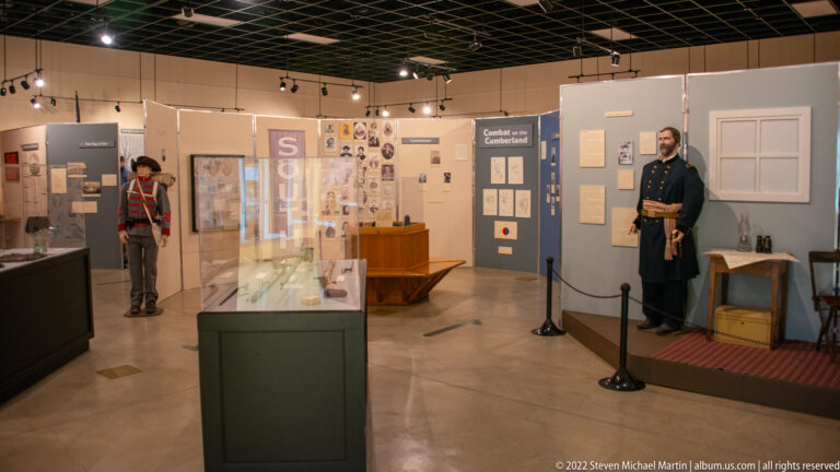Museum gallery with display cases, wall panels and two Civil War mannequins standing on opposite sides.