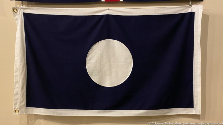 A dark blue flag with a single large white circle hangs against a pale wall.
