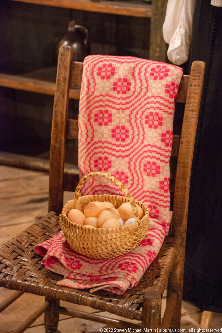Basket of pale eggs rests on red patterned fabric on a woven chair.