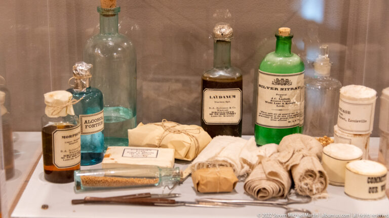 Glass bottles, wrapped medical bundles and metal instruments arranged in a museum case.