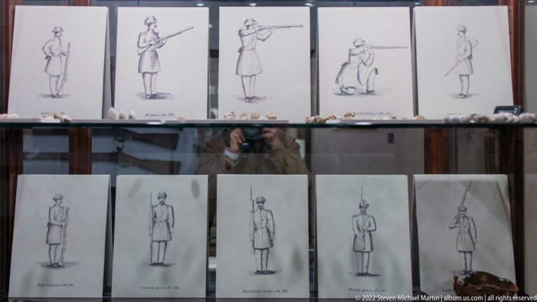Rows of soldier drawings show different uniform views and poses behind glass.