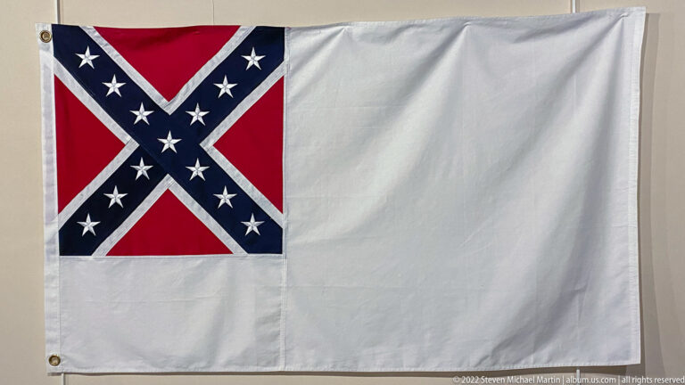 A white flag has a red-and-blue starred cross in its upper-left corner.