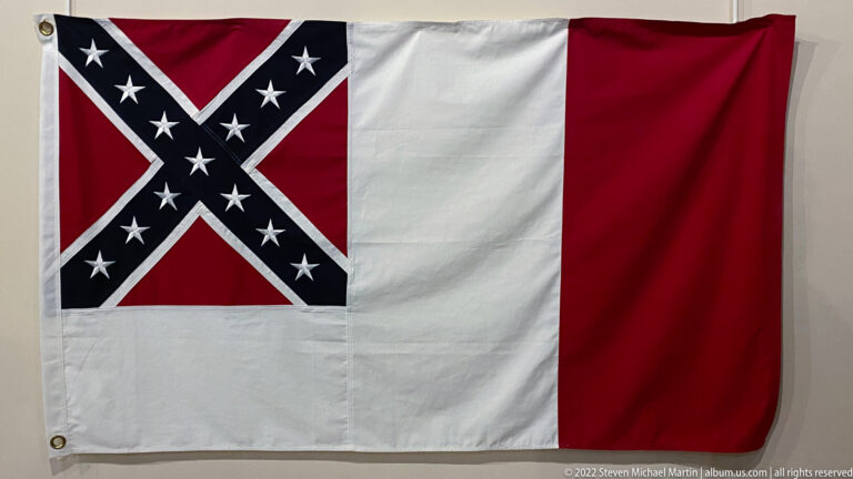 A red-and-white flag bears a white-edged blue diagonal cross with white stars.