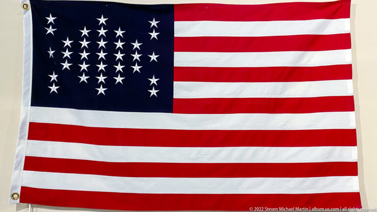 A United States flag with red and white stripes has 34 stars arranged in a circle on blue.