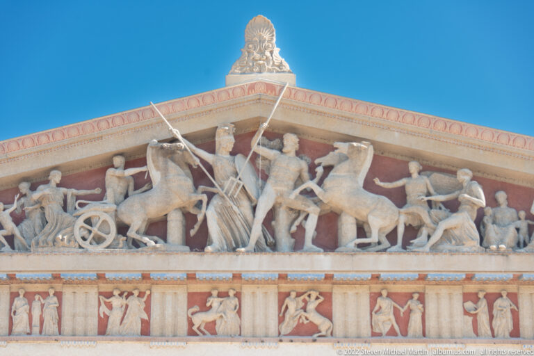 A chariot and standing figures fill the pediment above a band of painted scenes.