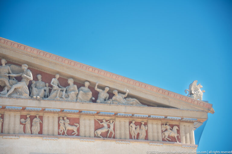 Figures extend along the sloping pediment above a row of painted panels.