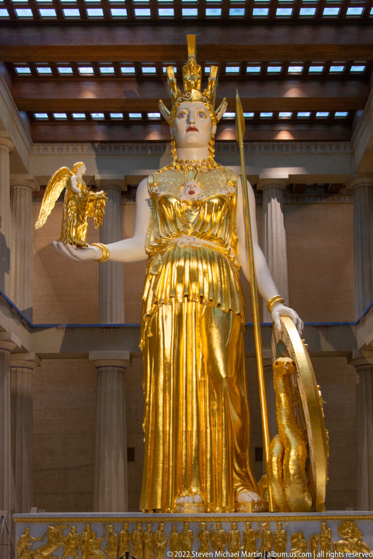 Athena faces forward holding a small winged figure and spear, with a shield at her side.