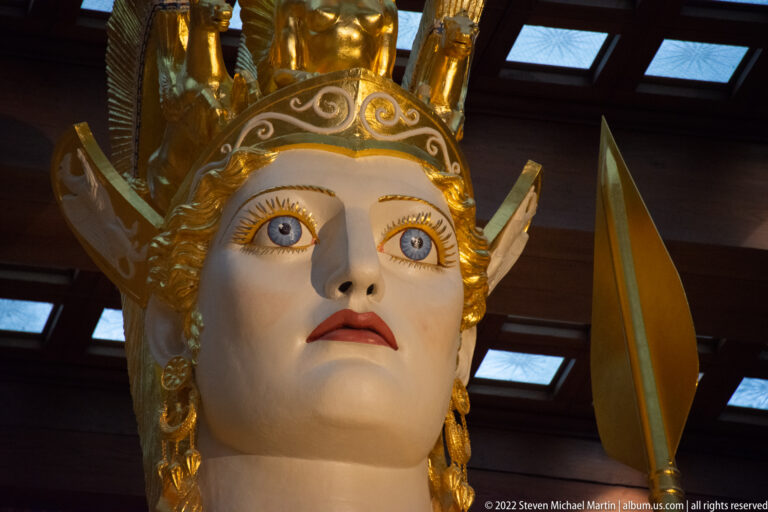 Athena’s painted face and gilded helmet fill a low-angle view beneath the roof lights.