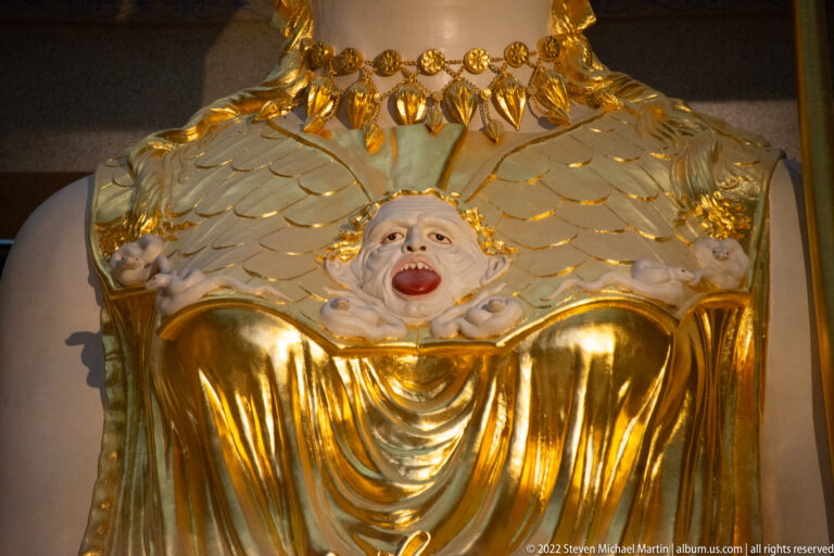 A small open-mouthed face appears at the center of Athena’s gilded breastplate.