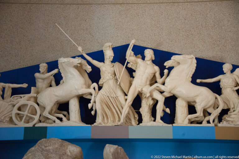 A draped figure stands among horses and attendants in a shallow sculptural group.