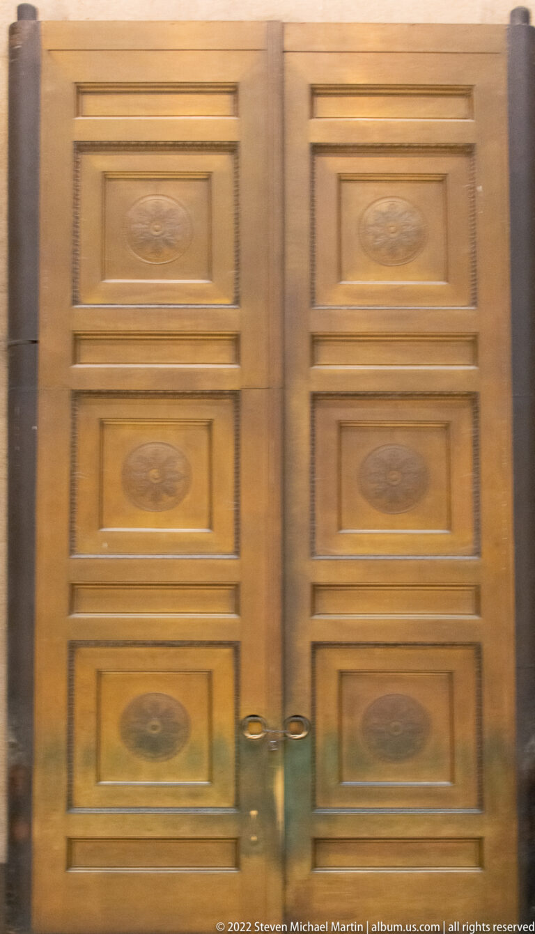 Closed pair of brown paneled doors with oval medallions and symmetrical rectangular moldings.