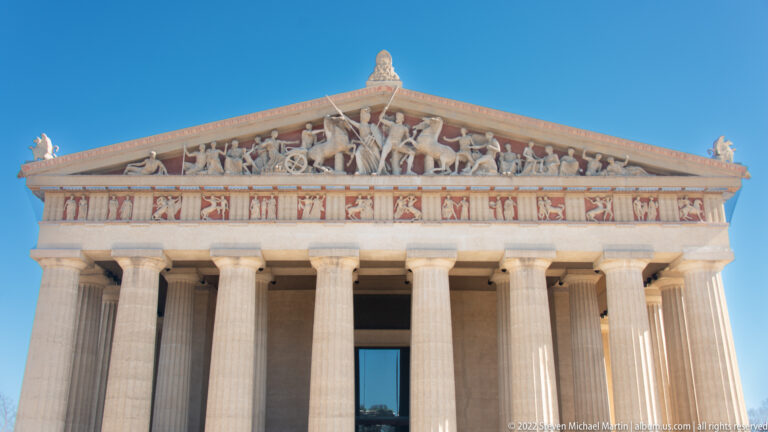 A sculpted triangular pediment and painted frieze sit above the temple’s entrance columns.