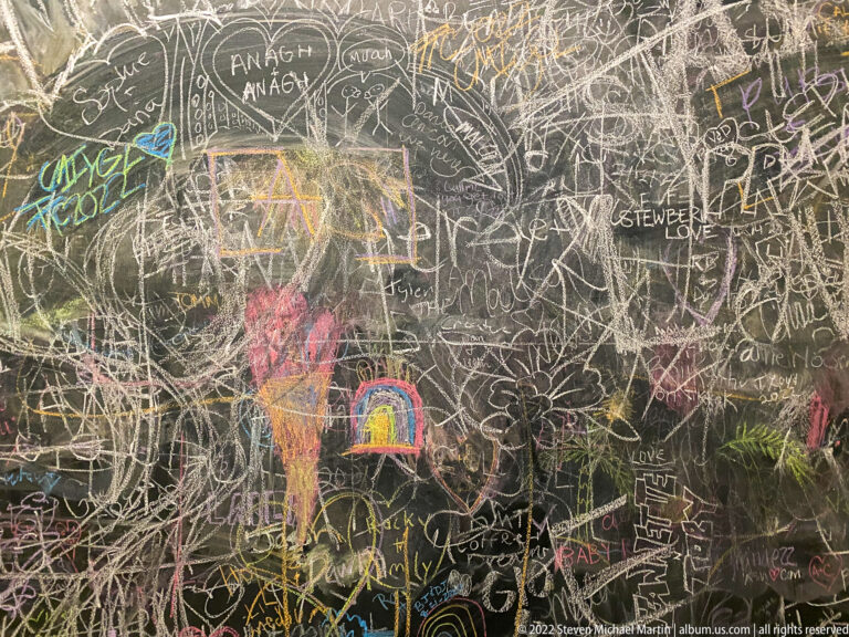 Handwriting, names, sketches, and colorful chalk drawings cover the dark wall from edge to edge.