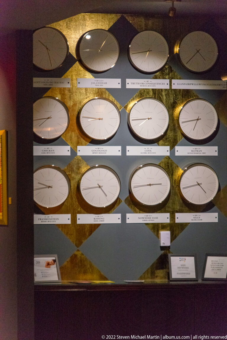 Rows of round clocks with dark hands and labels fill a framed wall display.