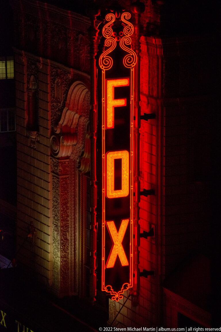 A vertical red FOX neon sign glows on the ornate stone facade of a theater at night.