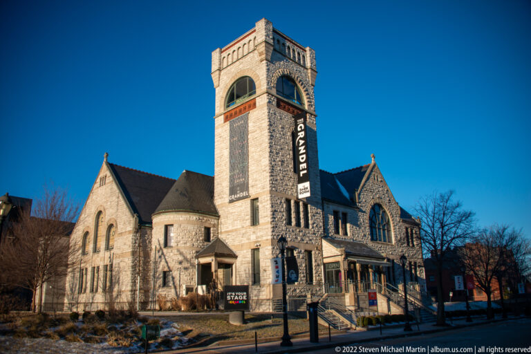 The stone Grandel Theatre stands beneath a blue sky, with its tower sign and arched windows visible.