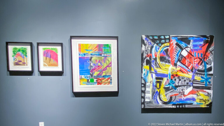 Two small framed prints, a larger colorful work, and a black-ground abstract painting form a gallery display.