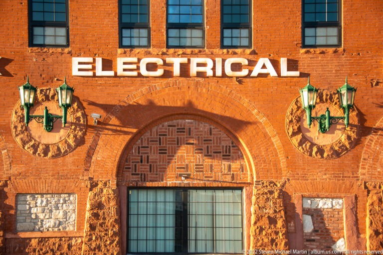 Orange-brick façade with large “Electrical” lettering, arched entrance and matching green lamps.