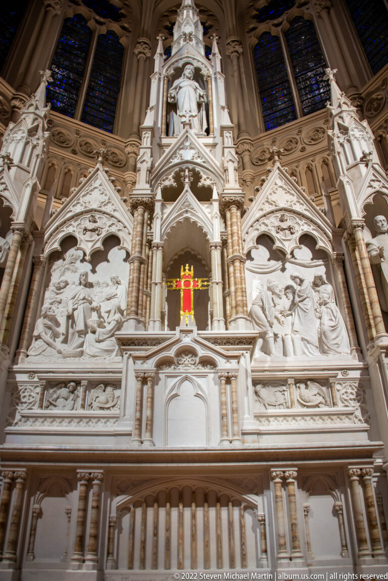 Pale carved altarpiece rises in pointed tiers with niches, figures and relief panels.