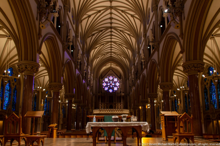 Cathedral nave leads toward a distant rose window and altar beneath ribbed vaults.