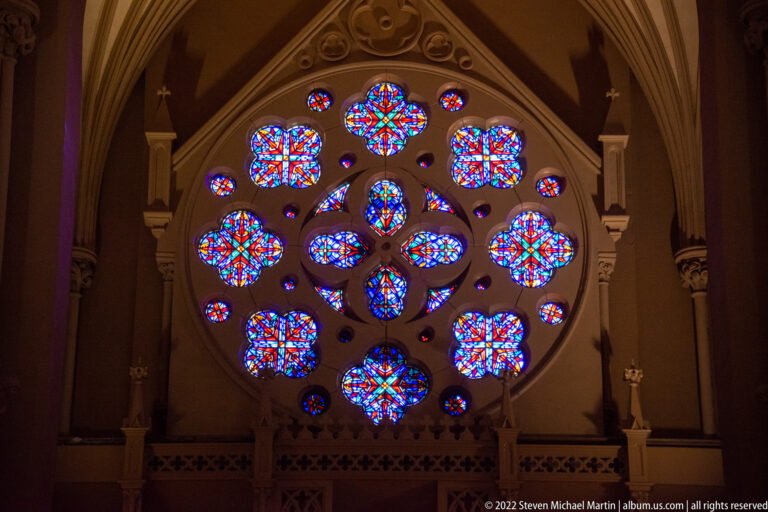 Colorful circular rose window with a radial pattern set within a pointed stone arch.