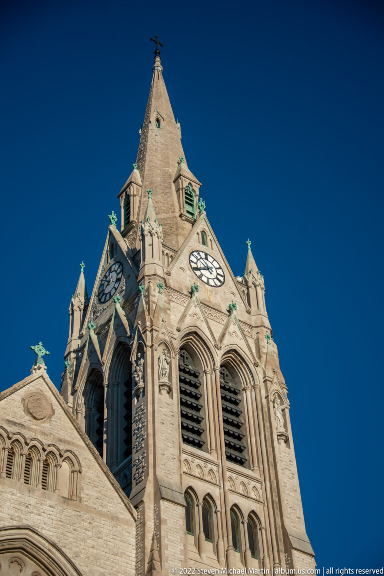 Low-angle detail of cathedral tower with twin clocks, pointed openings and carved stonework.