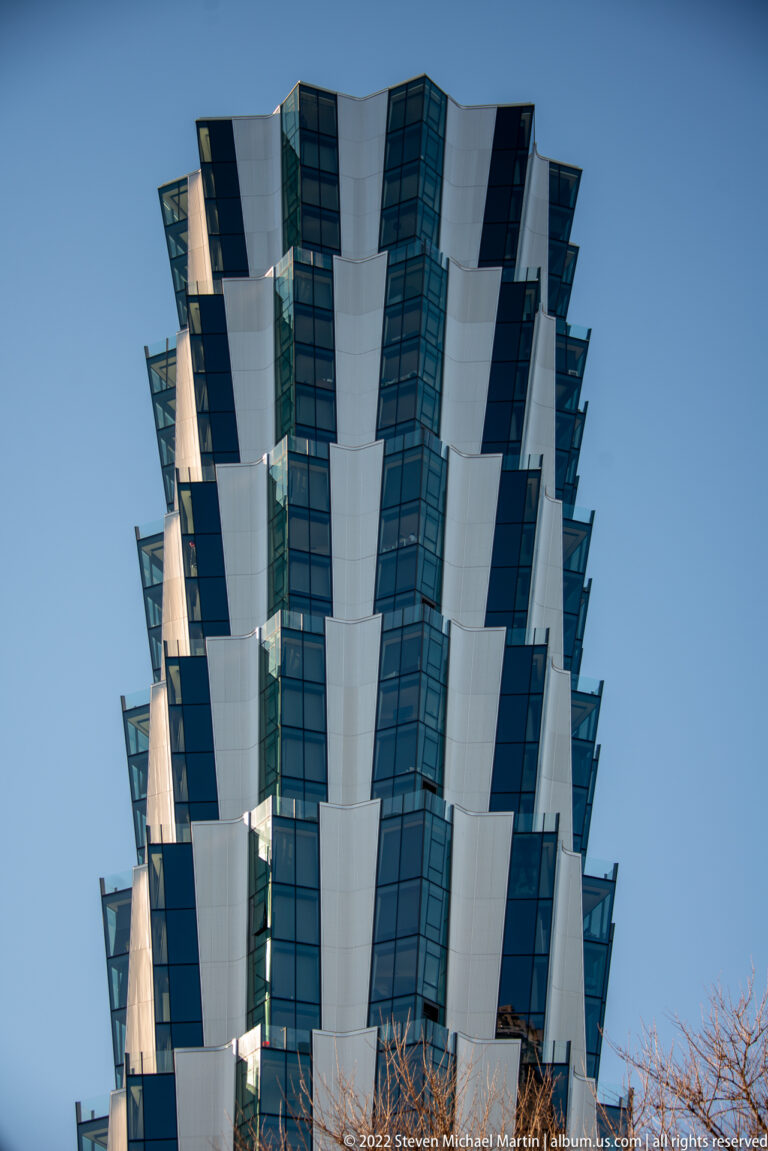 Modern building with stacked projecting white panels and dark blue glass windows.