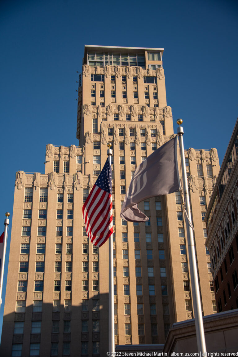 Tan high-rise with rows of windows behind an American flag and pale banner.