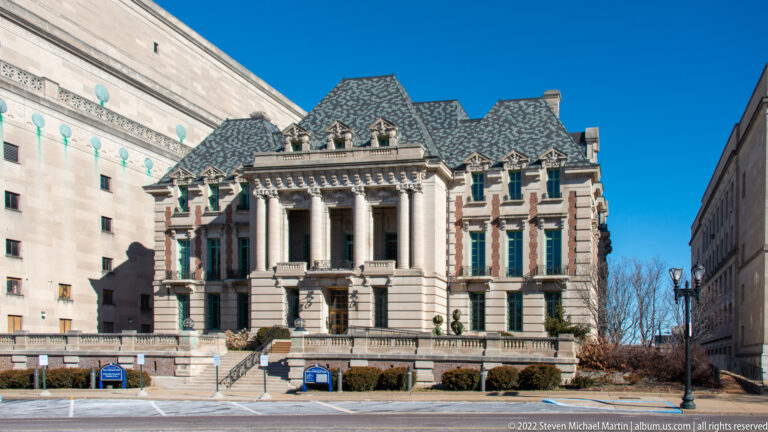 Historic stone building with a columned portico, carved pediment and steep patterned roofs.