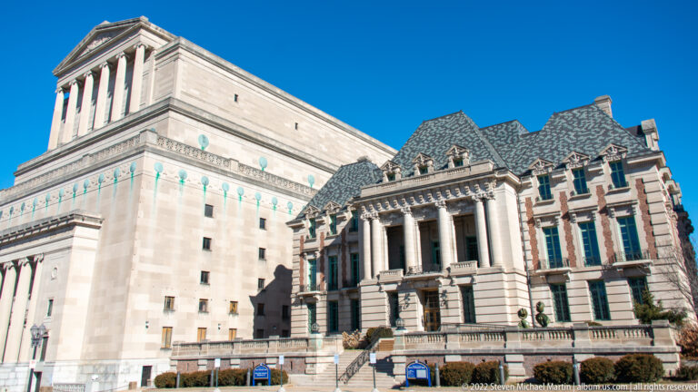 Columned historic building centered between taller downtown blocks in bright winter sun.