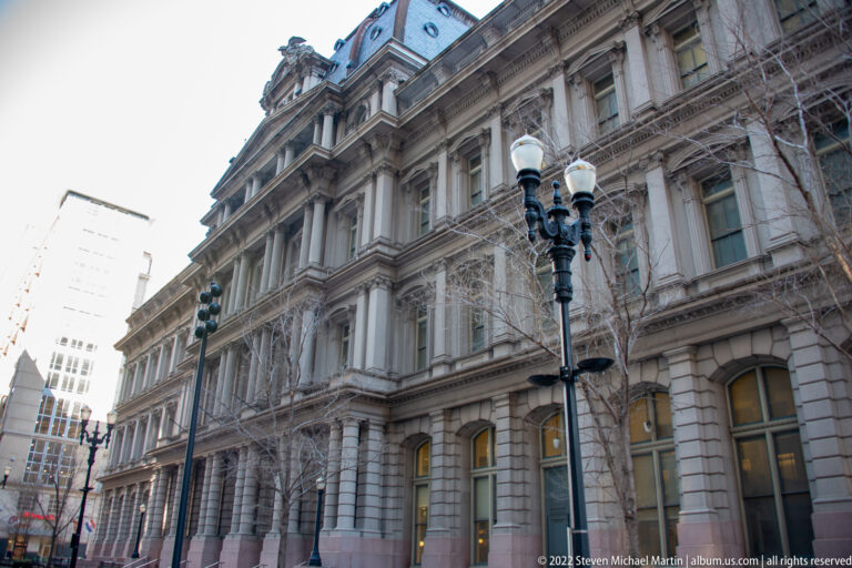 Ornate stone building with rows of windows, a mansard roof and a double-headed streetlamp.
