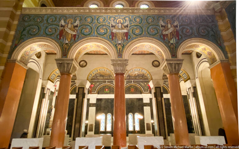 Mosaic figures and circular motifs run above a row of arches and columns along the cathedral wall.